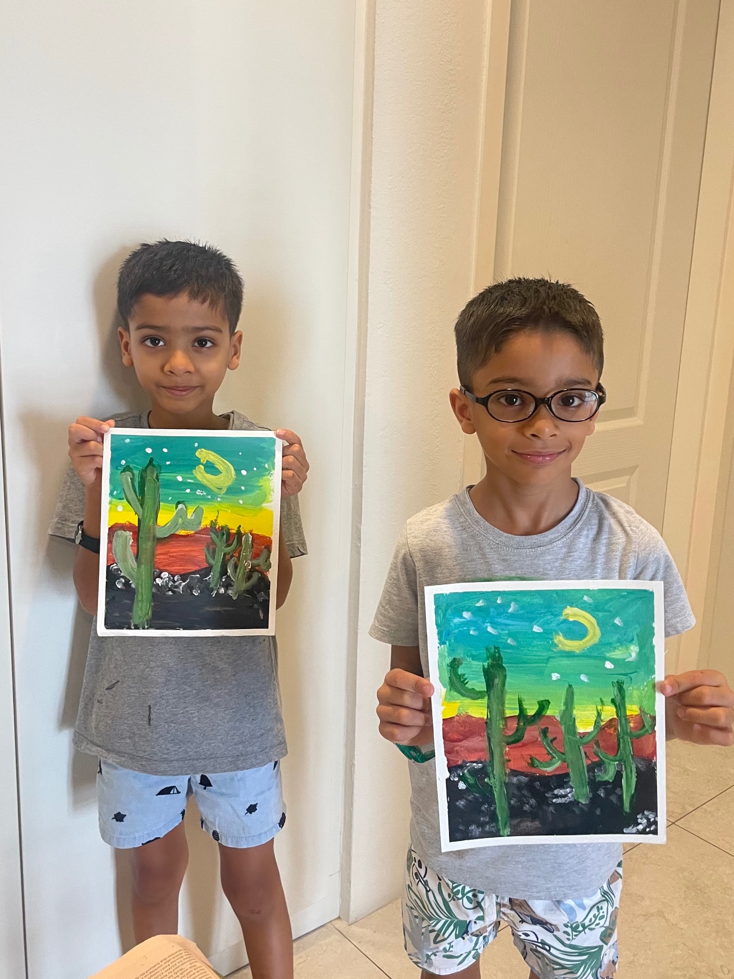 Two young students proudly holding their cactus sunset paintings