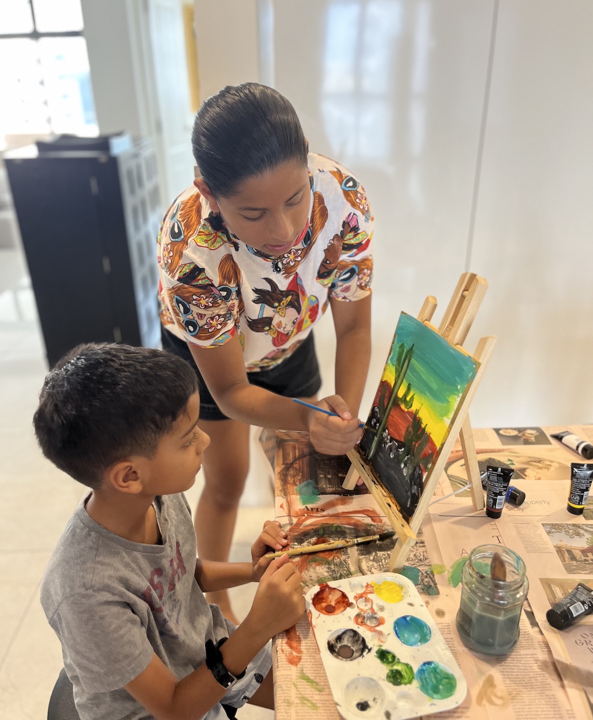 Sania teaching a young student to paint a cactus landscape