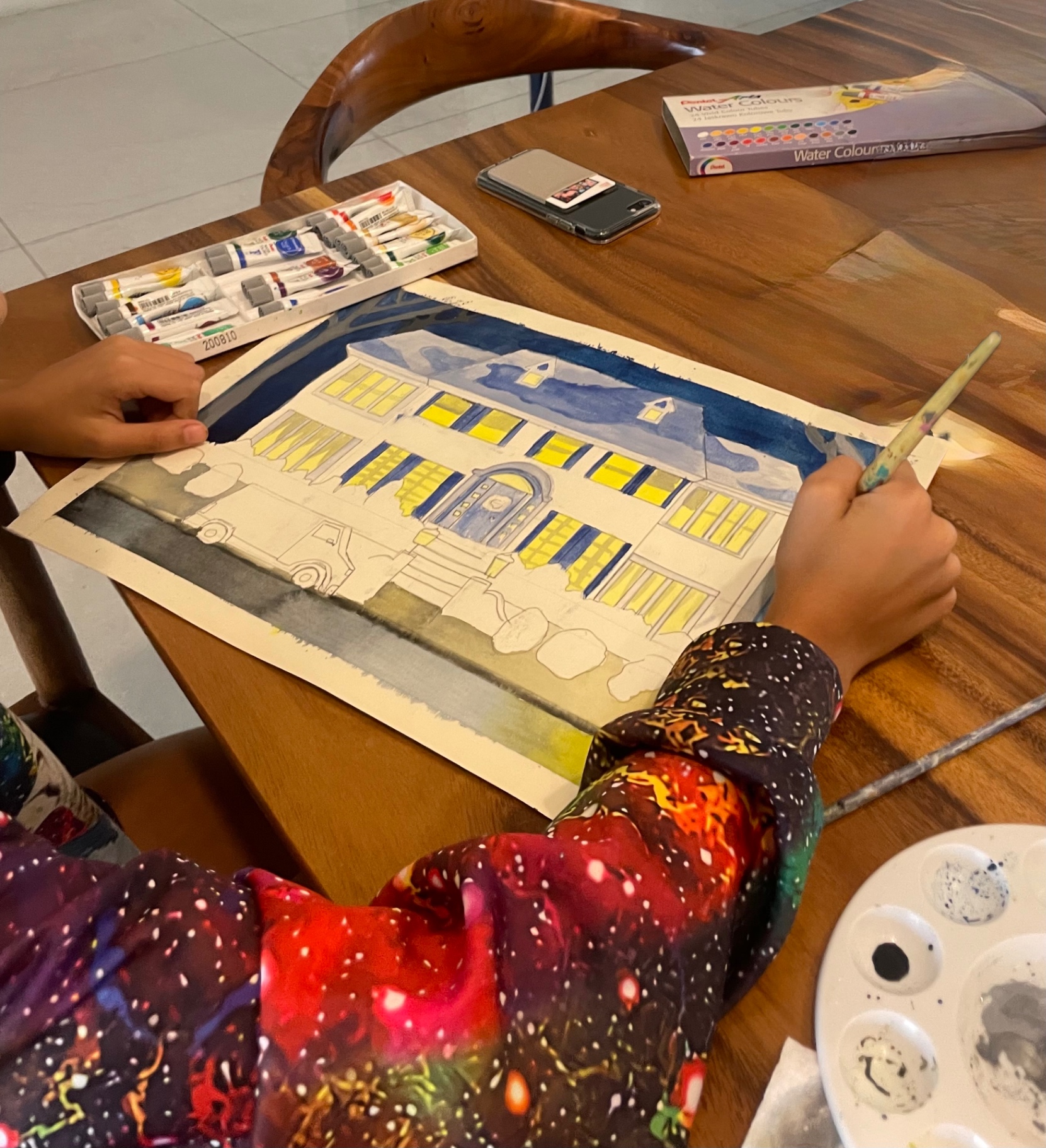 Student painting a watercolor of a brick house at night