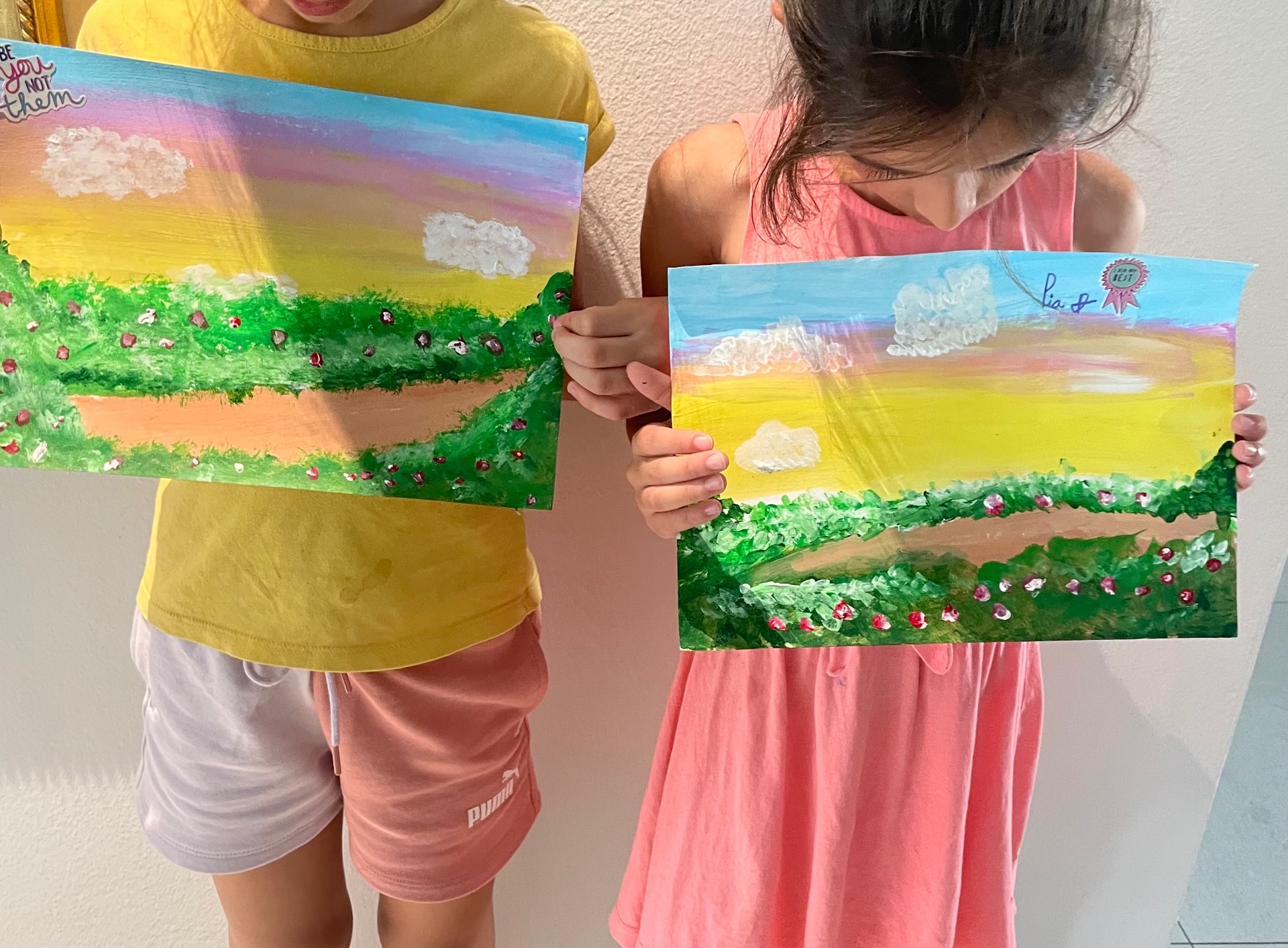 Two students holding pastel meadow landscape paintings