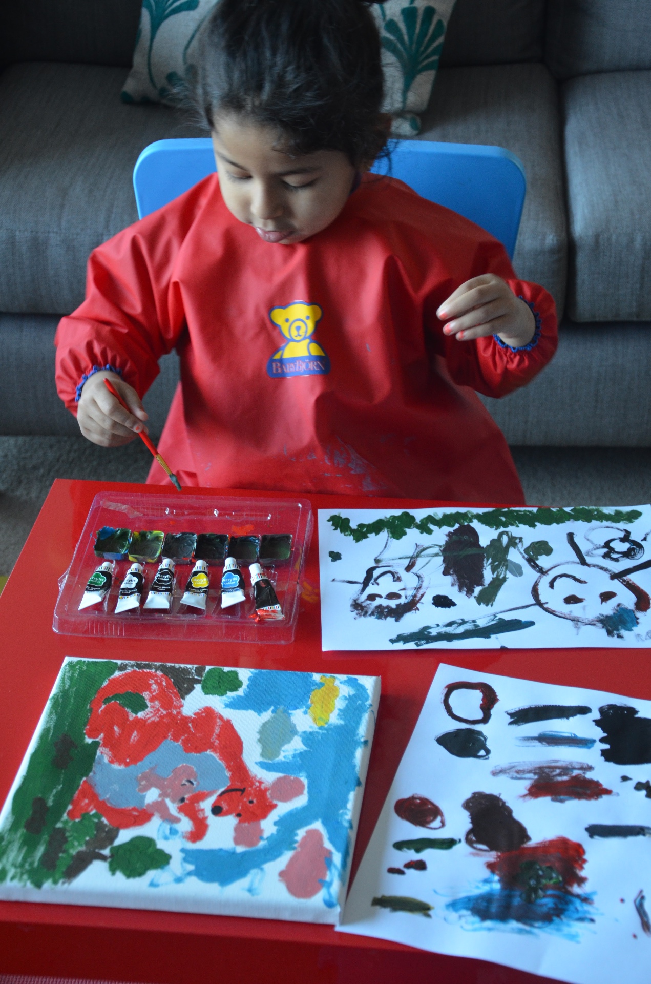 Young Sania painting at a small red table with her artwork spread around her