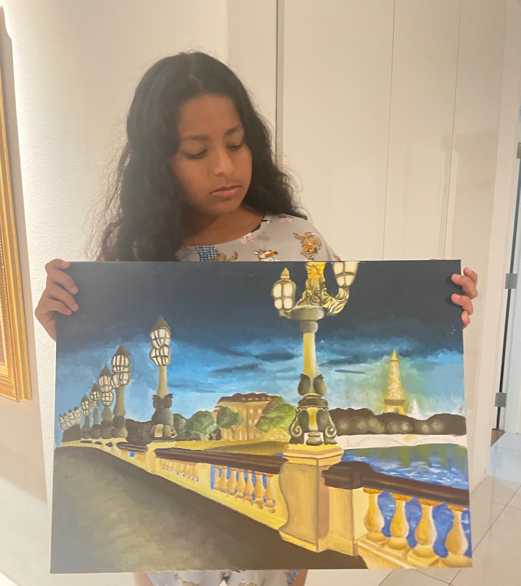 Sania holding her oil painting of the Pont Alexandre III bridge in Paris