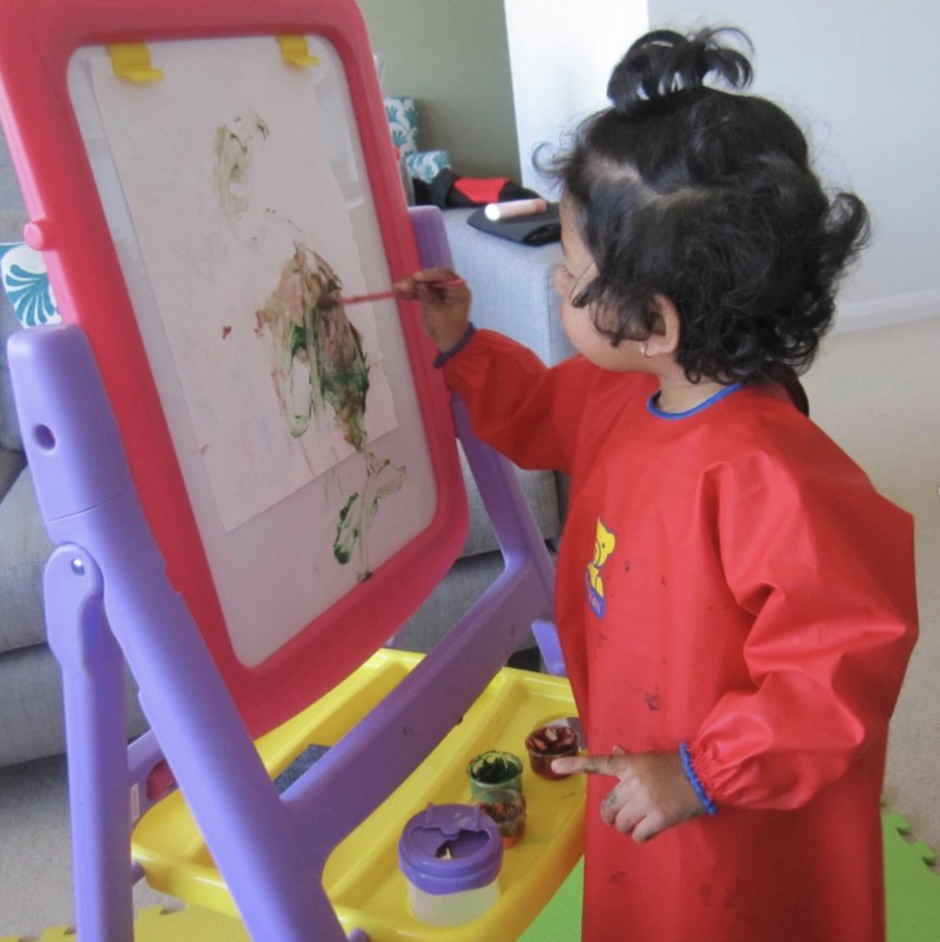 Sania as a toddler painting at her pink and purple easel